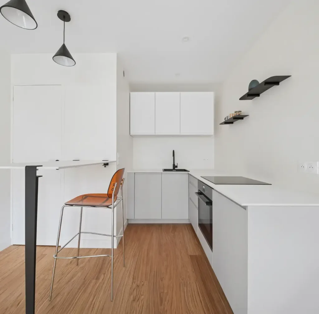 Cuisine avec table haute, murs et mobiliers blanc, luminaires noir mat et parquet bois clair