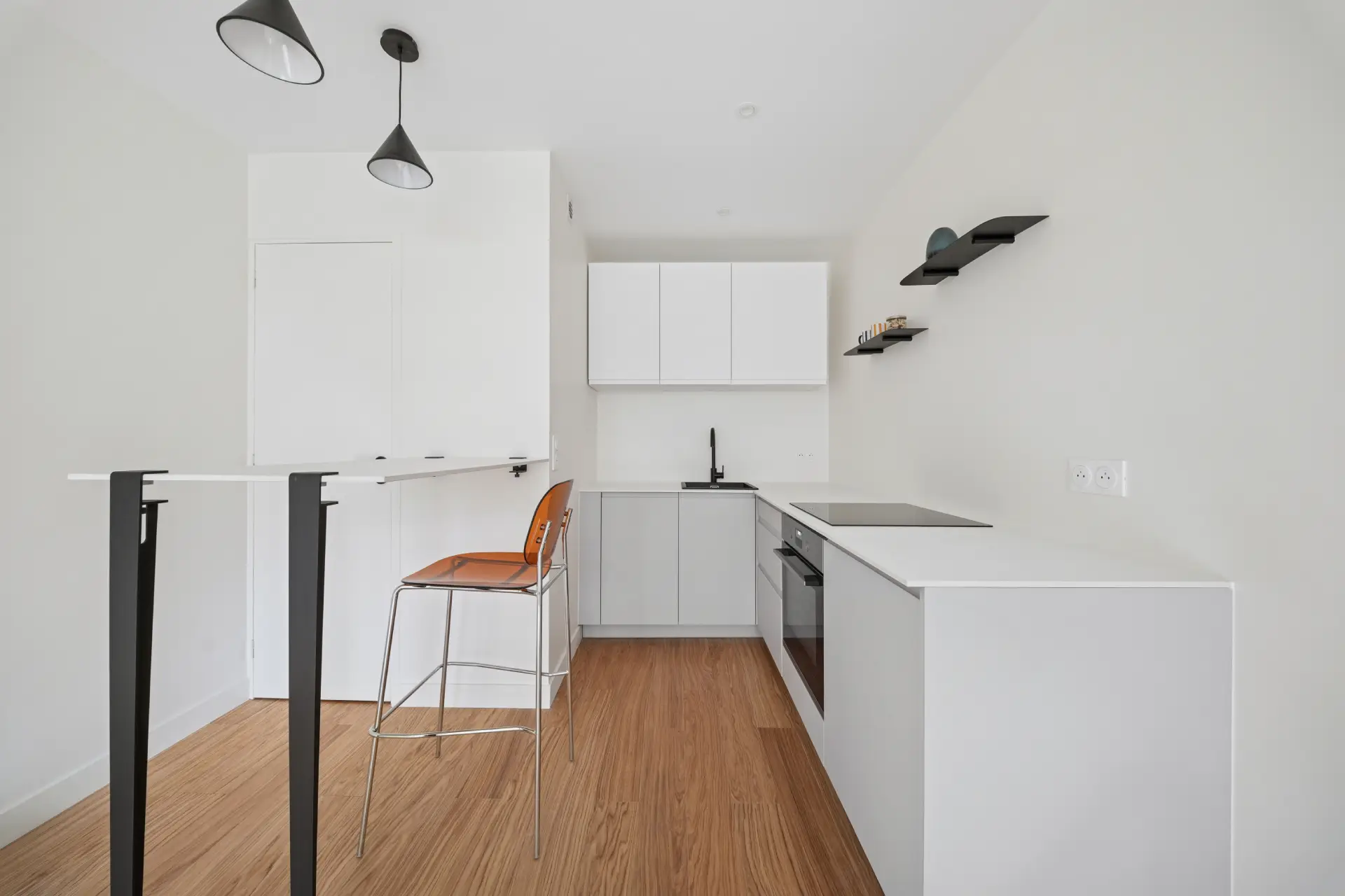 Cuisine avec table haute, murs et mobiliers blanc, détails noir mat et parquet
