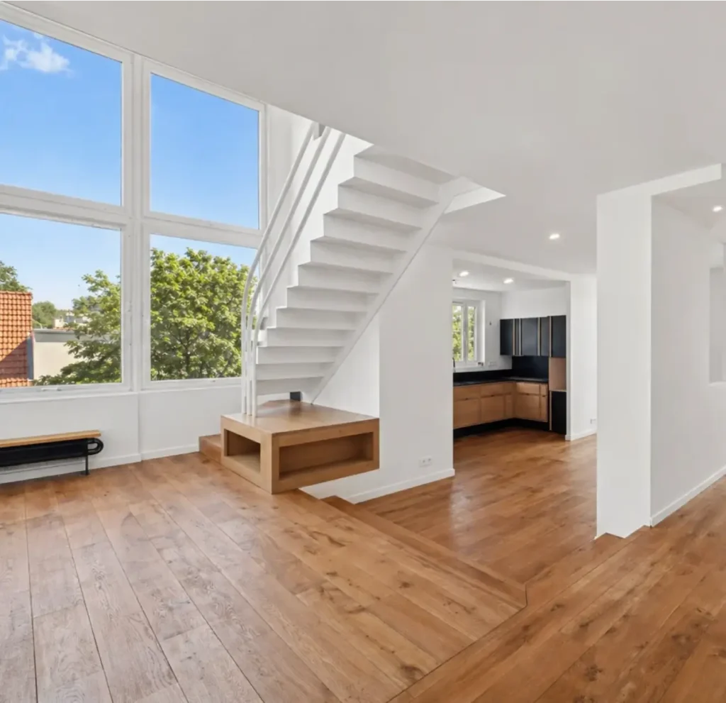 Duplex vide après rénovation, vue sur le séjour avec grandes fenêtres, escaliers et cuisine