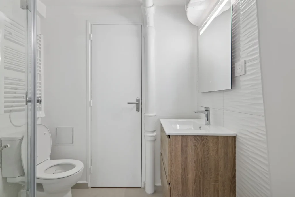 Salle de bain attenante au studio, murs blanc avec mobilier en bois