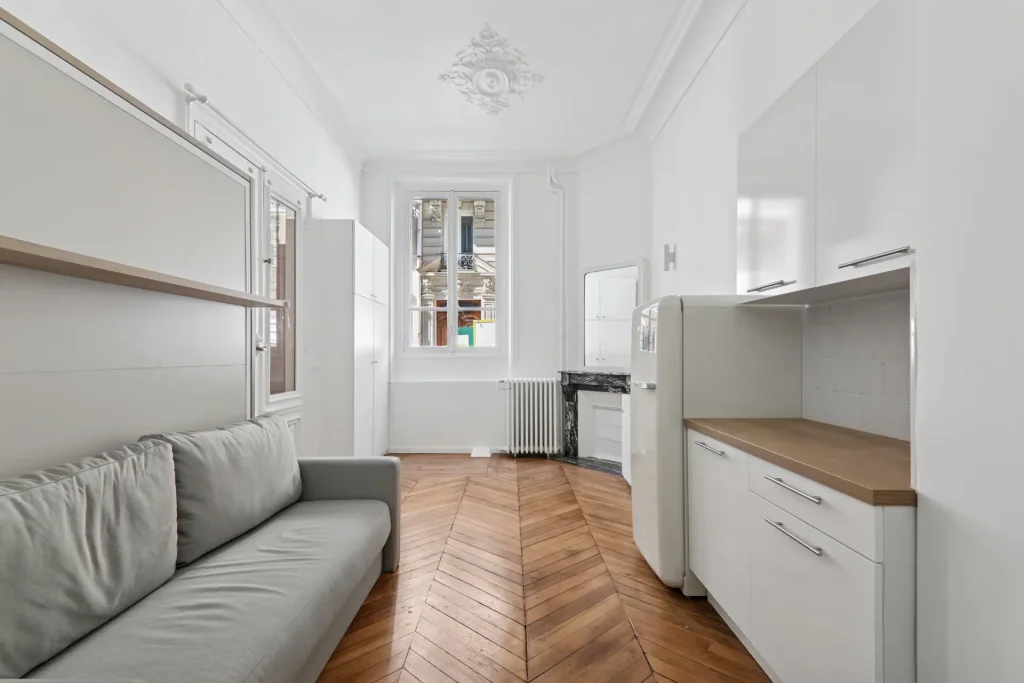 Vue complète du studio rénové à Paris 16, avec vue sur l'espace cuisine, séjour et cheminée